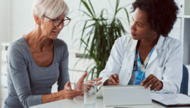 A female doctor sits at her desk and chats to an elderly female patient while looking at her test results