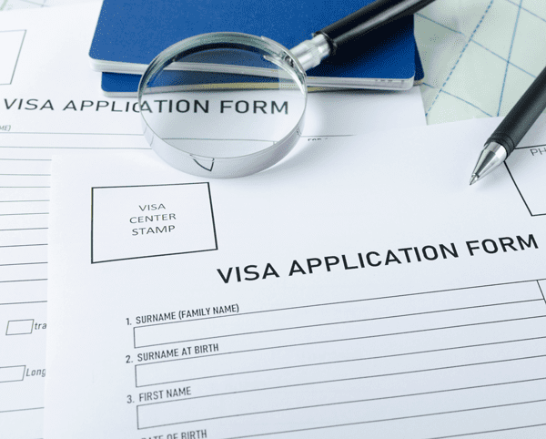 Closeup of blank visa application form, passports, pen and magnifyng glass on the map.